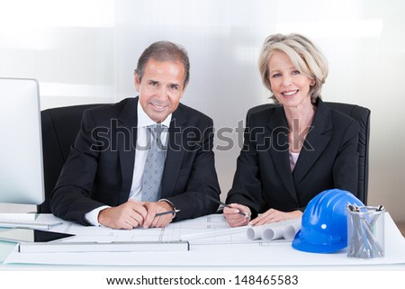 Mature Engineers Looking At Plans Sitting At A Table