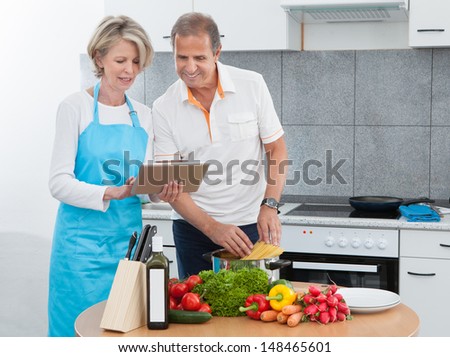 Mature Man And Woman Looking At Recipe Tablet While Cooking In Kitchen