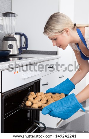 Young Woman Placing Tray Full Of Cookies In Oven