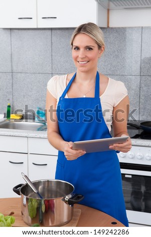 Woman Using Digital Tablet In Kitchen For Recipe