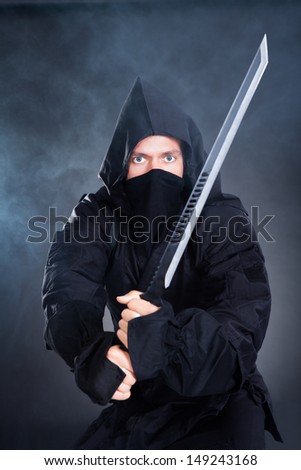 Portrait Of Male Ninja In Black Costume Holding Sword