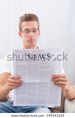Portrait Of Young Man Reading Newspaper Sitting On Couch
