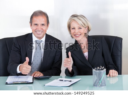 Mature Businessman And Businesswoman Showing Thump Up Sign In Office