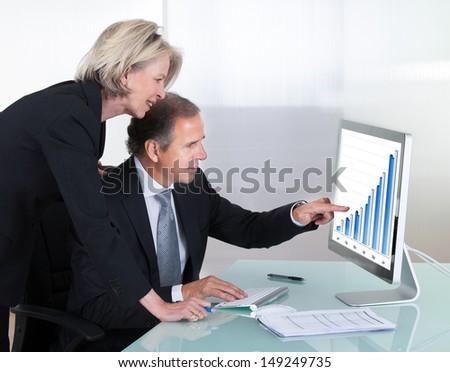 Happy Mature Businessman And Businesswoman Looking At Graph On Computer