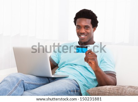 Happy Young African Man Using Laptop Sitting On Couch At Home