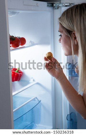 Young Woman Eating Cookies From Refrigerator At Night