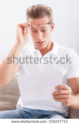 Shocked Young Man Reading Paper Holding In Hands