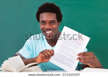 Happy African Male Student Showing A Paper With Perfect Grade A Plus In Classroom