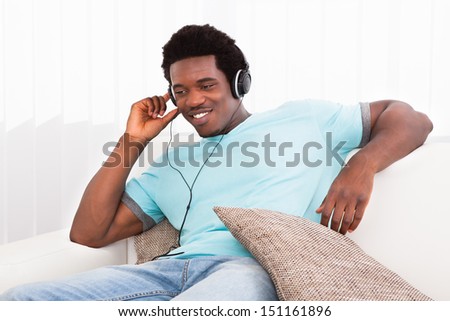 Happy Relaxed Young African Man Sitting On Couch Listening Music On Headphone
