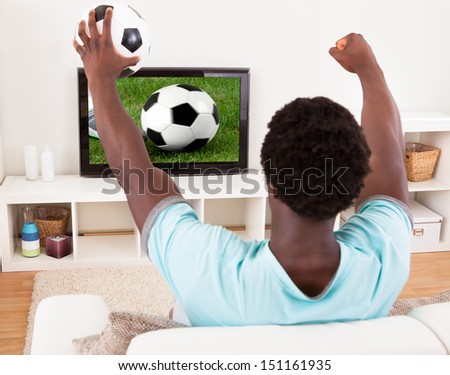 Happy African Young Man Watching Football Match In Television At Home