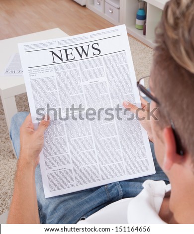 Portrait Of Young Man Reading Newspaper Sitting On Couch