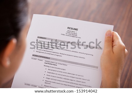 Close-up Of Young Businesswoman Reading Resume At Desk