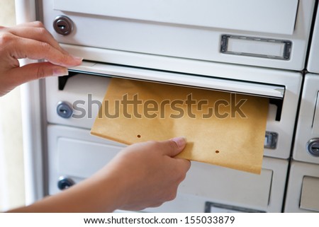 Close-up of woman's hand holding envelope and inserting in mailbox