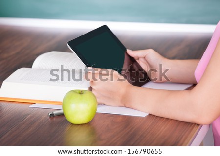 Student with apple and book on desk holding digital tablet