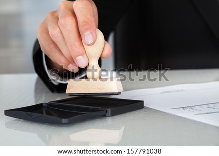 Close-Up Of Business Man Hand Pressing Rubber Stamp On Document
