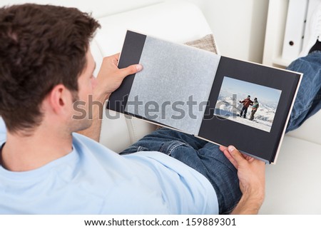 Young Man Sitting On Couch Looking At Photo Album