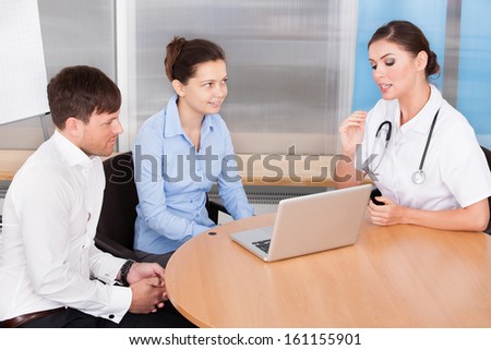 Happy Young Couple Having Appointment With Female Doctor At Clinic