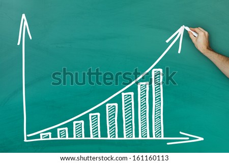 Hand holding chalk writing profit growth chart on green blackboard