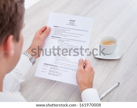 Close-up Of Businessman Reading Resume With Tea Cup On Desk