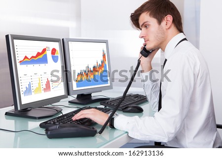 Stock Broker Using Telephone Sitting In Front Of Desktop