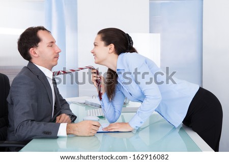 Naughty Businesswoman Holding Necktie Of Young Businessman