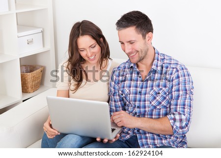 Portrait Of A Happy Young Couple Sitting On Couch Using Laptop