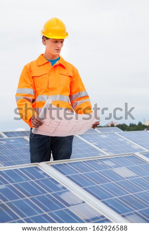 Portrait Of A Male Engineer Holding Blue Print With Solar Panel Around