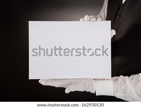 Closeup Of Young Waiter Presenting Blank Placard Over Black Background