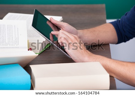 Male Student Surrounded By Books Using Digital Tablet