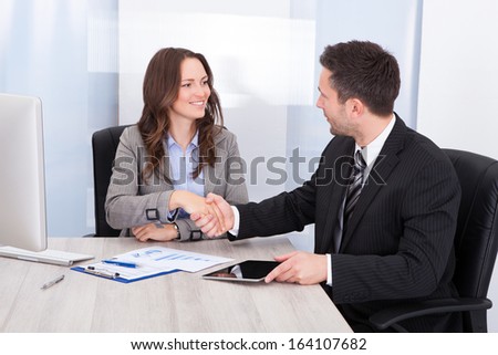 Businesswoman Looking At Businessman While Shaking Hand At Office Desk