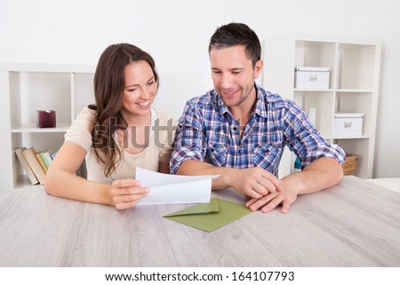 Portrait Of A Happy Young Couple At Home Reading Paper