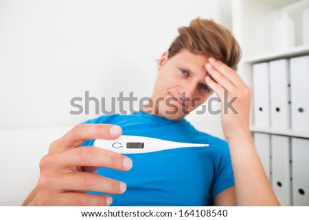 Man Suffering From Fever And Measuring Temperature With Thermometer