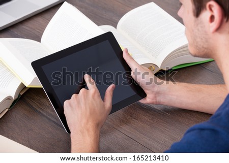 Male Student Surrounded By Books Using Digital Tablet