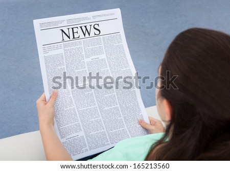 Rear View Of A Woman Sitting On Couch Reading Newspaper