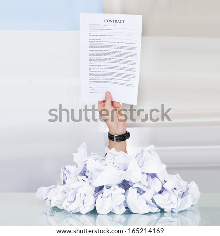 Person Under Pile Of Crumpled Paper Holding Contract Paper