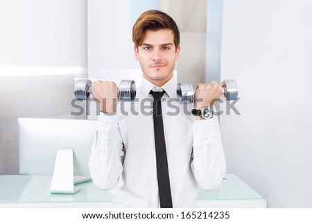 Handsome Young Businessman Exercising With Dumbbells At Office