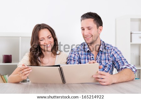 Portrait Of Happy Couple Sitting Side By Side Looking At Photo Album