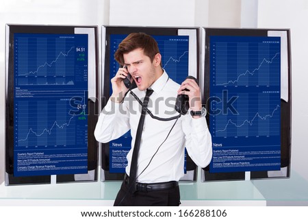 Furious Young Stock Broker Talking On Telephone In Front Of Computer Screen