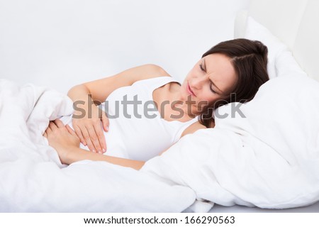 Portrait of woman with stomach ache lying on bed