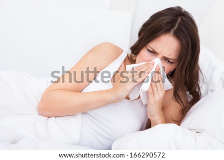 Young Woman Lying On Bed Infected With Allergy Blowing Her Nose