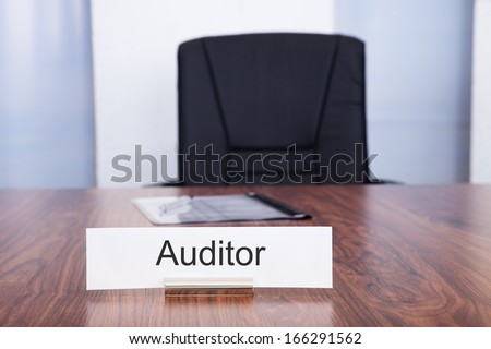 Nameplate With Auditor Title Kept On Desk In Front Of Empty Chair
