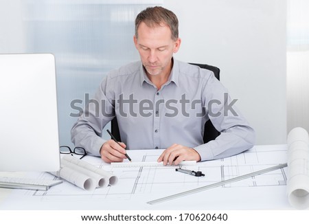 Portrait Of A Mature Architect Drawing Plan On Blueprint In Office