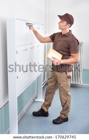 Portrait Of Mature Postman Putting Letters In Mailbox