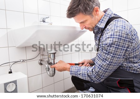 Mature Male Plumber Fitting Sink Pipe In Bathroom