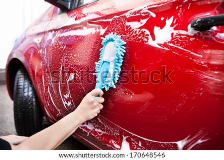 Close-up Of Hand With Blue Brush Washing Red Car