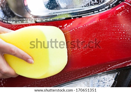 Close-up Of Hand Washing Red Car With Yellow Sponge