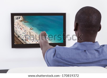Rear View Of African Man Changing Channel With Remote