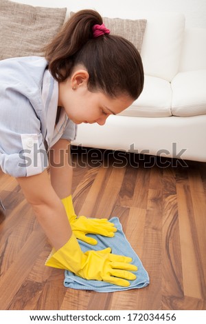 Portrait Of Young Maid Cleaning Hardwood Floor With Cloth