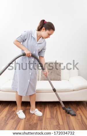 Young Maid Cleaning Floor With Handheld Vacuum Cleaner