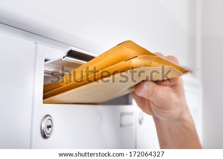 Close-up Of Postman Putting Letters In Mailbox